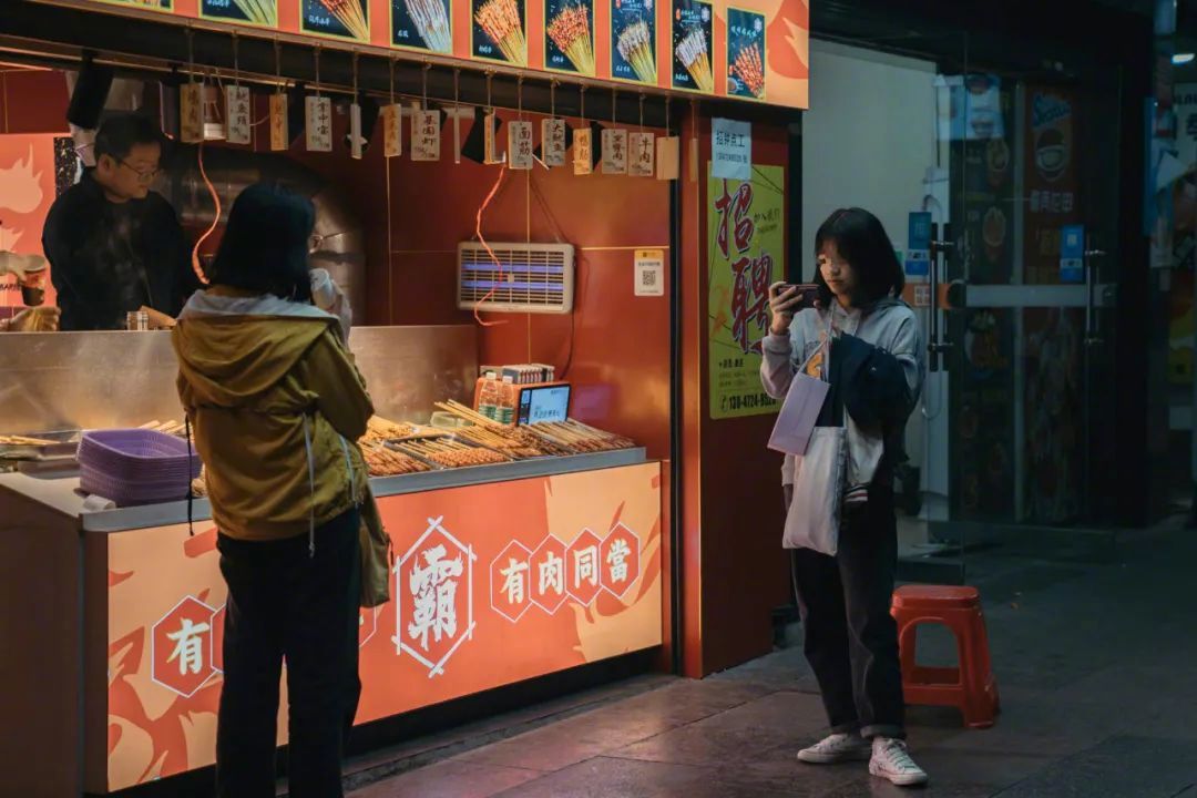 祁东县城里，小吃摊和奶茶店是少年们最主要的社交场所。图为一名女孩在摊位前刷着短视频